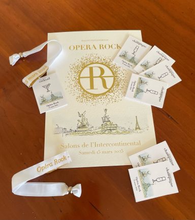 Déclinaison du design Opéra de Paris sur bracelet & coupon coupe de champagne Brochure de l'hôtel avec échantillons de produits cosmétiques autour, sur une surface en bois.